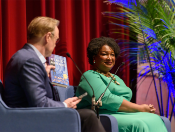 Stacey Abrams in green dress smiles at an interviewer holding her book, "While Justice Sleeps", on stage at the 2024 New Orleans Book Festival at Tulane University.