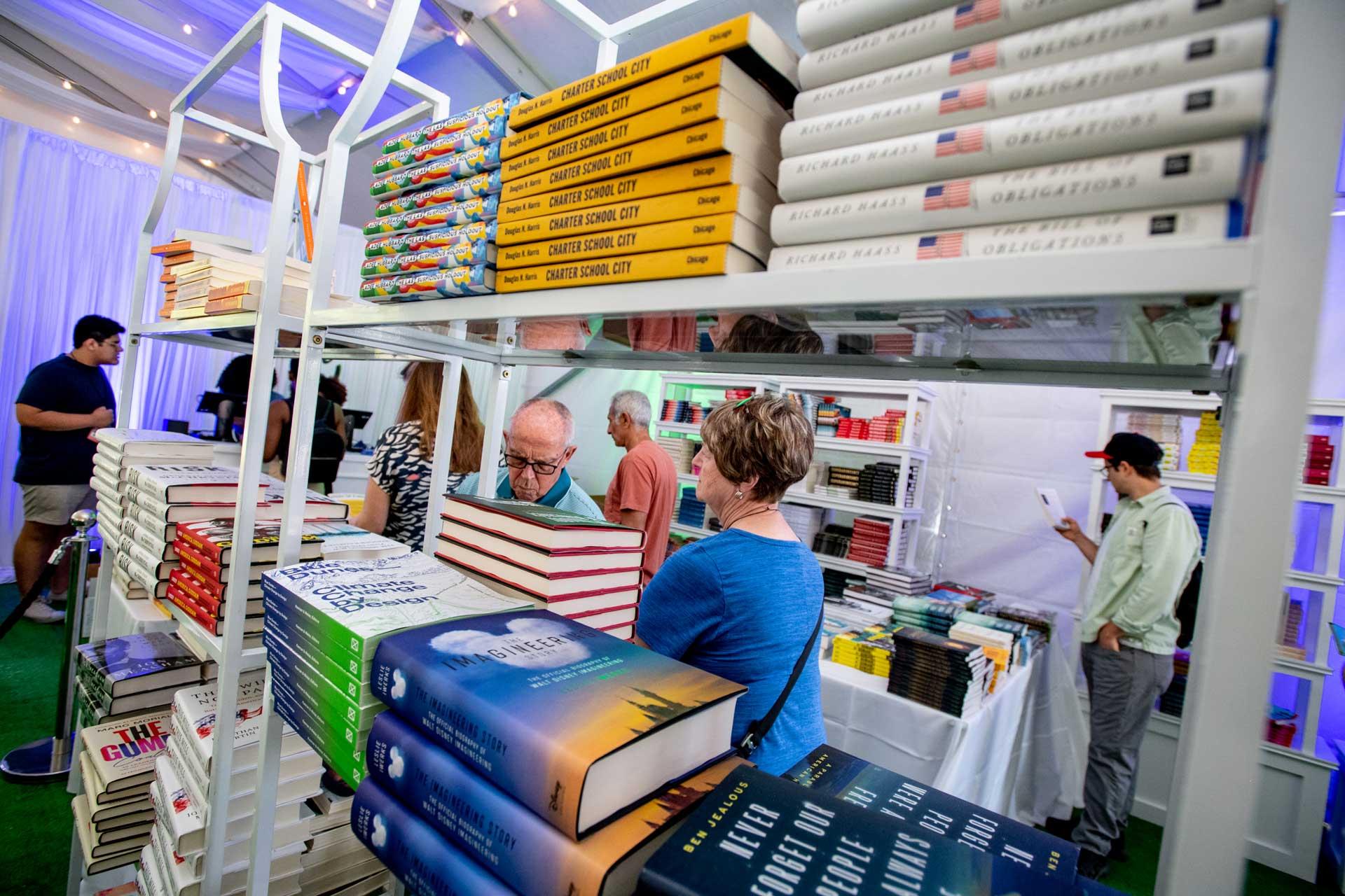 People tour the aisles of books in a book fest tent. 