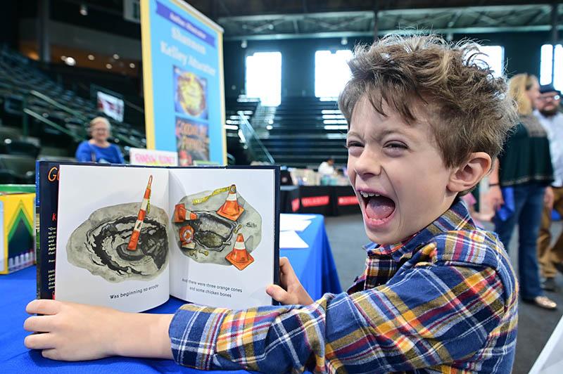 Max Powers at the 2024 New Orleans Book Festival enjoys a book about New Orleans potholes at Family Day at the Fest.