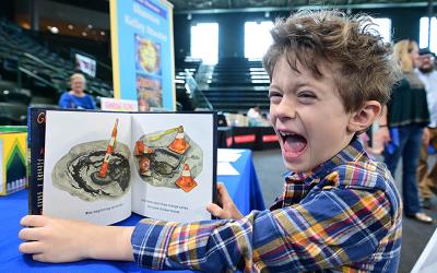 Max Powers at the 2024 New Orleans Book Festival enjoys a book about New Orleans potholes at Family Day at the Fest.