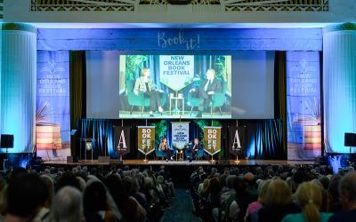 Audience watching a panel discussion on stage at a book festival in a large hall.